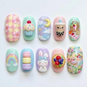 May include: A set of ten decorative nail art pieces featuring various raised designs including a yellow plaid pattern with pink flowers, a cupcake, a crescent moon, a boba tea, a picnic basket, a rainbow, stacked macarons, a rabbit, a berry tart, and floral cakes.