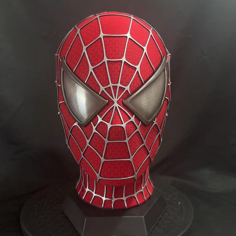 May include: A red full-head mask featuring a raised silver web pattern across the entire surface. The mask includes two large, angular, metallic silver eye lenses with a smooth finish, designed to cover the eyes completely in a classic superhero style.