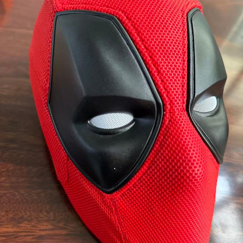 May include: A red full-head mask featuring a textured mesh fabric surface. The mask includes two large, angular black eye frames surrounding white mesh eye lenses, creating a distinct facial appearance with a bold, vibrant red color scheme.