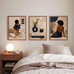 May include: Three framed wall art prints displayed above a bed. The left print shows a person reading a book. The center print features white lilies in a black vase on stacked books with text. The right print depicts a person in a dark dress.