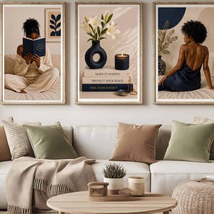 May include: A triptych of framed wall art prints displayed above a white sofa with beige and sage green pillows. The left print shows a person reading, the center print features white lilies in a black vase and books, and the right print shows a person.