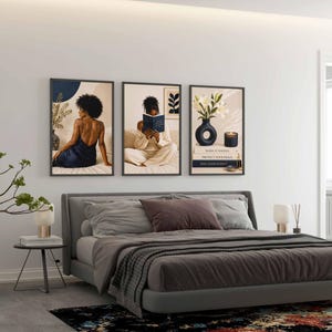 May include: A set of three framed wall art prints displayed above a bed. The first print shows a person in a dark blue dress, the second shows a person reading a book, and the third features a vase with white flowers, a candle, and stacked books.