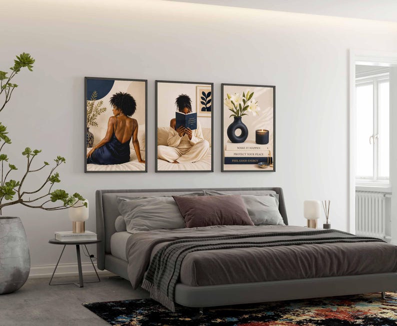May include: A set of three framed wall art prints displayed above a bed. The first print shows a person in a dark blue dress, the second shows a person reading a book, and the third features a vase with white flowers, a candle, and stacked books.