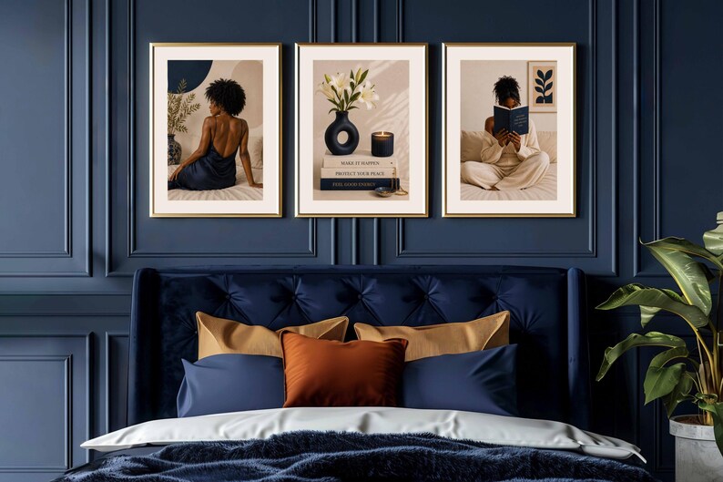 May include: A set of three framed wall art prints featuring a person in a dark dress, a vase of white lilies with books and a candle, and a person reading a book. The prints are displayed in gold frames against a dark blue paneled wall.
