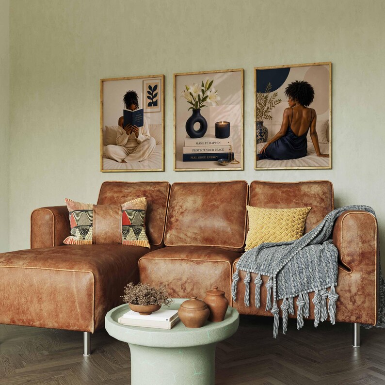 May include: A brown leather sectional sofa with a patterned pillow, a yellow textured pillow, and a gray tasseled throw blanket. A round light green coffee table sits in front with two small bowls and books. Three framed wall art prints.