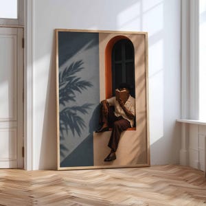 May include: A framed wall art print depicting a person sitting in an arched window frame reading a book. The scene features a blue wall with a palm leaf shadow, a beige wall, and a dark window shutter. The person wears a light shirt and dark trousers.