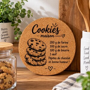 Può includere: Un sottopentola rotondo in sughero con una grafica stampata in nero che raffigura una pila di quattro biscotti con gocce di cioccolato. Il testo recita: Cookies maison, 200 g de farine, 100 g de sucre, 100 g de beurre, 1 œuf, Pépites de chocolat et bonne humeur! con icone a forma di cuore.