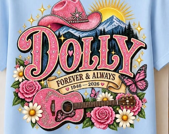 Puede incluir: Una camiseta azul claro con un estampado gráfico de un sombrero de vaquero rosa, una guitarra acústica rosa, flores, mariposas y un paisaje montañoso. El texto dice DOLLY FOREVER & ALWAYS 1946-2026 con pequeños corazones alrededor de las fechas.