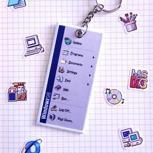 May include: A blue and white keychain with a Windows 98 start menu design. The keychain features a blue and white start menu with options for Update, Programs, Documents, Settings, Find, Help, Run, Log Off, and Shut Down. The keychain also includes a small, white, pixelated start button with the word "Start" in black.