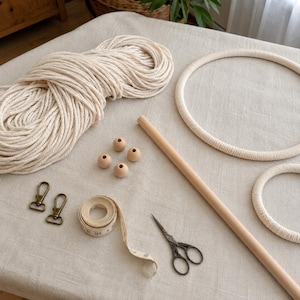 Pu&ograve; includere: Un kit per macram&egrave; composto da una grande matassa di corda di cotone color bianco sporco, due anelli metallici circolari rivestiti in corda, un bastoncino di legno liscio, quattro perline di legno, due moschettoni in bronzo, un metro a nastro e forbici.