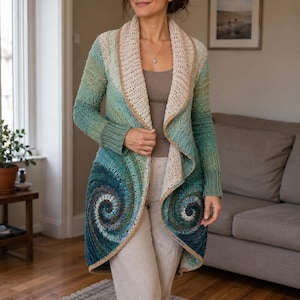 Op de afbeelding: Een gehaakt vest met lange mouwen in een kleurverloop van blauwgroen, blauw en groen. Het kledingstuk heeft twee opvallende spiraalpatronen op de onderste voorpanden, een brede crèmekleurige sjaalkraag en geribbelde boorden in blauwgroen.