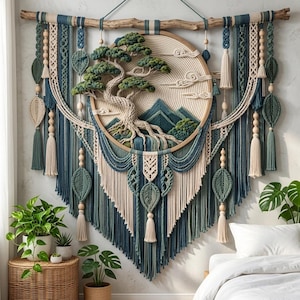 May include: A large macrame wall hanging suspended from a driftwood branch, featuring a central circular hoop with a textured fiber art bonsai tree and mountain landscape in shades of cream, sage green, and teal, accented with wooden beads and tassels.