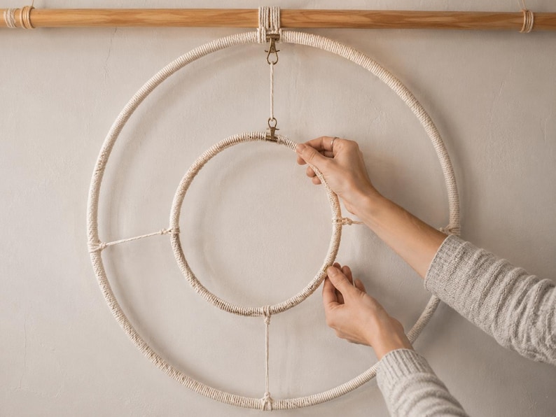 Pu&ograve; includere: Una decorazione da parete composta da due anelli in macram&egrave; color bianco sporco concentrici, sospesi a un bastone di legno orizzontale. L'anello esterno pi&ugrave; grande e quello interno pi&ugrave; piccolo sono collegati da cordini e clip metalliche.