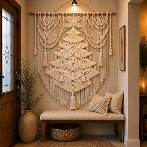 Puede incluir: Un gran tapiz de macramé en color blanco roto con un diseño central de árbol de Navidad, nudos intrincados, lazos decorativos y borlas colgantes, suspendido de una vara de madera sobre un banco de madera en una pared neutra.
