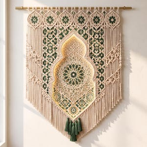 Op de afbeelding: Een grote macramé wandhanger van crèmekleurig koord met ingewikkelde knooppatronen en donkergroene accenten. Het ontwerp bevat een centrale boogvormige nis met een geometrisch stermotief, van binnenuit verlicht, en afgewerkt met kwastjes.