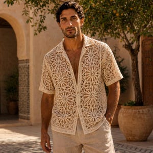 May include: A short-sleeved, button-down shirt made of cream-colored crochet fabric featuring a repeating circular floral pattern. The garment has a classic collar, a straight hem, and a semi-sheer construction, paired with light beige trousers.