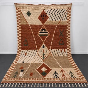 May include: A rectangular hand-knotted rug featuring a geometric pattern in shades of rust, beige, and dark green. The design includes diamonds, triangles, and linear motifs with a checkered border and a fringe of tassels along the bottom edge.