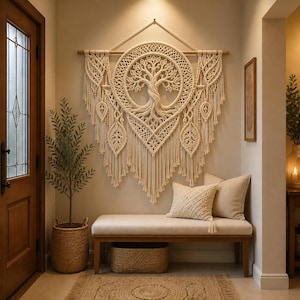 Puede incluir: Un gran tapiz de macramé en color blanco roto que presenta un diseño central circular de árbol de la vida con nudos intrincados, colgado de una varilla de madera. La pieza incluye detalles decorativos en forma de hoja y largos flecos.