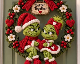 May include: A crochet wreath featuring two green characters in red and white outfits, sitting together and holding a red heart. The wreath is decorated with red berries, white flowers, and a sign that reads Better Together with a small red heart.