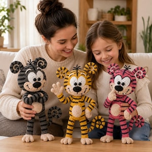 May include: Three crocheted tiger dolls with large round ears and curled tails. One doll is grey with black stripes, one is yellow with black stripes, and one is pink with black stripes. Each doll has a white face, black nose, and black eyes.