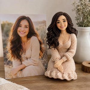 Puede incluir: Una muñeca de ganchillo hecha a mano con cabello de hilo marrón oscuro largo y un vestido de color beige claro de manga larga con dobladillo con volantes, junto a una fotografía rectangular de una persona con el mismo atuendo.