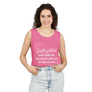 May include: A bright pink sleeveless tank top featuring white text that reads Gaslit, gatekept, and still the smartest person in the room, surrounded by delicate white line art illustrations of roses, crescent moons, and small stars.
