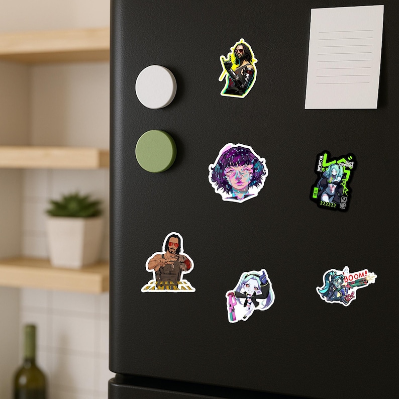 May include: A black refrigerator door featuring six assorted stickers including a man with a robotic arm, a portrait with purple hair, a character with green hair and Japanese text, a man with sunglasses, a small figure, and a character with a gun.