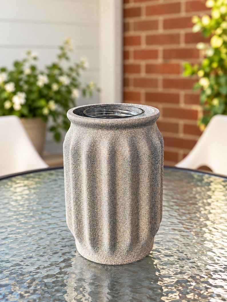 May include: A cylindrical vase with a textured, speckled gray stone-like finish and vertical fluted grooves. The vase features a wide, open top with a smooth, clear glass insert visible inside the center, creating a contrast in material and texture.