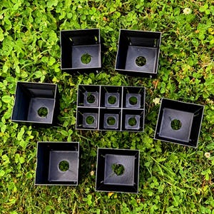 May include: A collection of black plastic square plant pots, including four individual larger pots and one connected tray containing six smaller square compartments, each featuring a circular drainage hole at the base of the container.