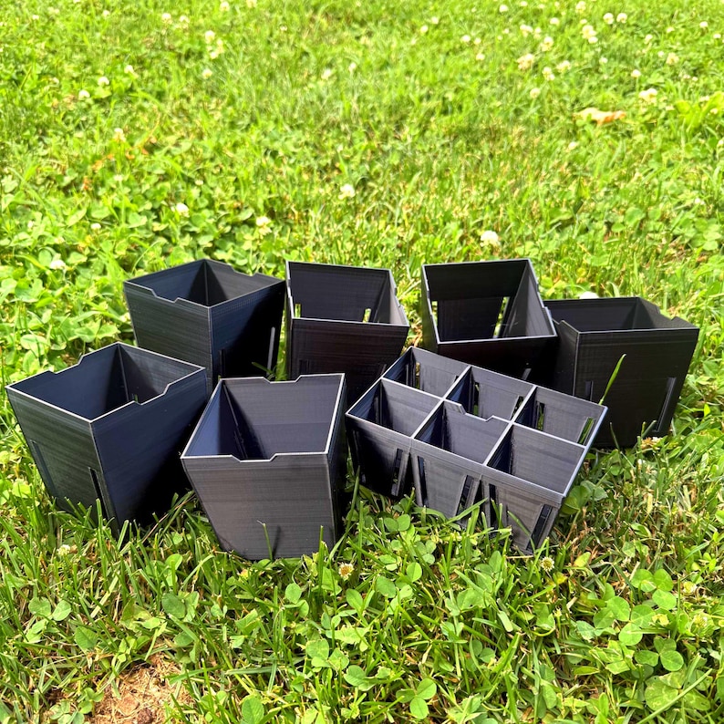 May include: A collection of dark gray, square-shaped plastic plant pots, including several individual containers and one multi-cell tray with six compartments, all featuring vertical side slits and open tops for gardening and seedling propagation.