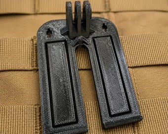 以下が含まれることがあります： 上部中央に3本爪の取り付けポイントを備えた黒いU字型の取り付けブラケット。表面はテクスチャ加工された層状の仕上げで、2つの長方形の凹型パネルと上端近くに2つの小さな円形の穴があります。
