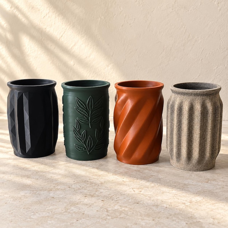 May include: Four cylindrical containers arranged in a row. The first is matte black with a geometric faceted surface. The second is dark green with embossed leaf patterns. The third is terracotta orange with a spiral twist. The fourth is beige with vertical fluted ridges.