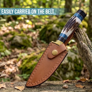 May include: A fixed-blade knife with a textured antler handle, blue accents, and a brass bolster, encased in a tan leather sheath with a brass snap closure. The text CAN BE EASILY CARRIED ON THE BELT is visible at the top of the image.