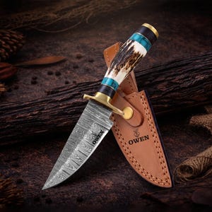 May include: A fixed-blade knife with a Damascus steel blade featuring the text OWEN, a brass bolster, and a handle made of antler and turquoise-colored material. The knife includes a tan leather sheath embossed with the text OWEN and a logo.