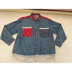 Può includere: Una camicia in denim blu a maniche lunghe con colletto e pannelli sulle spalle a motivo floreale rosso. Presenta due tasche sul petto, una floreale rossa e una floreale blu scuro, entrambe rifinite con pizzo bianco e frange di pizzo sull'orlo.