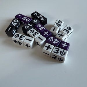 Peut inclure: Un ensemble de petits dés de jeu cubiques noirs, blancs et violets. Chaque dé présente des symboles imprimés, notamment des signes plus et moins, des chiffres et une icône de bouclier stylisée. Les dés sont disposés en un groupe lâche, montrant diverses combinaisons de ces marquages sur leurs faces visibles.