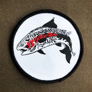 May include: A white embroidered patch with a black and red fish design. The fish is jumping out of the water and has a detailed pattern on its body.