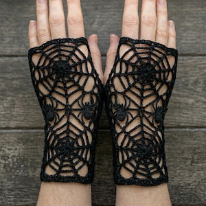 May include: A pair of black fingerless gloves featuring an intricate crocheted spiderweb pattern. Each glove is crafted with a delicate openwork design that incorporates small, three-dimensional spider motifs integrated into the web structure.