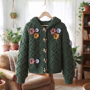 May include: A dark green knit hooded cardigan featuring a diamond cable pattern, long sleeves, and four wooden toggle buttons. The front is decorated with several small, colorful crocheted flowers in shades of pink, yellow, and light blue.
