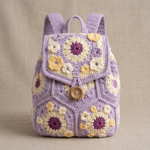May include: A lavender crochet backpack featuring a floral motif pattern made of hexagonal granny squares. The bag includes a flap closure secured by a single round wooden button, two shoulder straps, and a top handle, all in shades of purple, cream, and yellow.