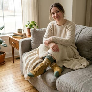 Può includere: Un paio di calze in maglia color giallo senape con un motivo a fiocco di neve bianco sulla parte superiore, polsini a coste verde salvia e punte verde salvia. Le calze sono realizzate in filato spesso e testurizzato e arrivano a metà polpaccio.