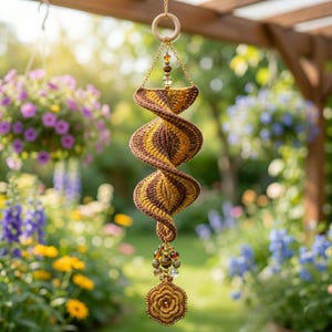 May include: A spiral-shaped crochet hanging ornament featuring alternating bands of brown and mustard yellow yarn. The piece is suspended by a gold-toned chain attached to a wooden ring and finished with a cluster of beads and a crocheted flower.