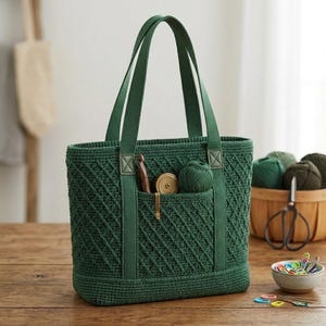 May include: A dark green crochet tote bag featuring a diamond-patterned texture, two sturdy fabric handles, and an exterior pocket containing a wooden crochet hook, a small circular metal gauge, and a ball of matching green yarn.