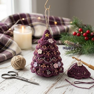 Può includere: Un ornamento per albero di Natale all'uncinetto color viola scuro con bordi smerlati a strati, accenti ricamati in filo metallico argento e rame, piccole perline e minuscoli fiori in tessuto. Una piccola stella gialla è cucita sulla punta.
