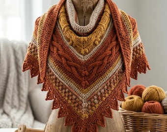 Può includere: Uno scialle triangolare all'uncinetto caratterizzato da un design a strati nei toni dell'arancione bruciato, giallo senape e crema. Il capo presenta intricati motivi a treccia, punti nocciolina testurizzati e un bordo smerlato.