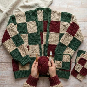 Könnte beinhalten: Eine Häkeljacke mit einem Schachbrettmuster aus dunkelgrünen, burgunderroten und beigen Quadraten. Das Kleidungsstück hat lange Ärmel, einen gerippten Saum und zwei Vordertaschen. Ein Knäuel burgunderrotes Garn, eine Holzhäkelnadel und ein Maßband.