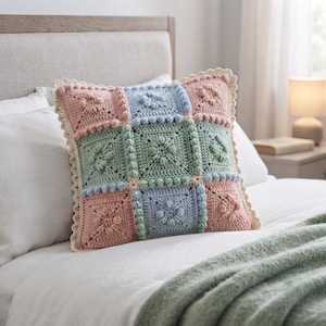 May include: A square crochet pillow featuring a grid of nine squares in alternating pastel pink, light blue, and sage green colors. Each square displays a central floral motif with raised bobble stitch textures and a scalloped crochet border.