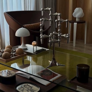 Peut inclure: Un candélabre en métal argenté à bras multiples, doté d'un pied central vertical et d'une base tripode, avec des articulations réglables et des bougeoirs cylindriques, posé sur une table en verre parmi divers objets de décoration intérieure.