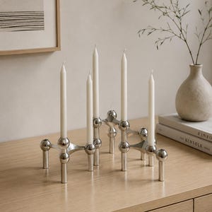 Peut inclure: Un bougeoir en métal argenté au design modulaire composé de sphères interconnectées avec plusieurs pieds et bras verticaux. Quatre bougies effilées blanches sont insérées dans les supports circulaires de la structure métallique polie.