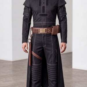 Op de afbeelding: Een zwarte jumpsuit met lange mouwen en witte contraststiksels, voorzien van geribbelde schouder- en kniepanelen, een bruine leren utility-riem met metalen gesp, een holster en een tasje, gecombineerd met een zilverkleurige metalen helm.
